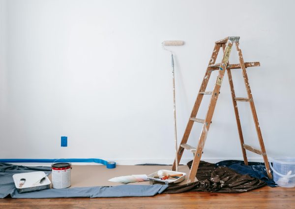 A room prepared for renovation with a ladder, paint supplies, and drop cloth.